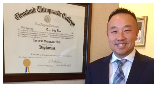 Dr. Dae Lee standing beside a framed Cleveland Chiropractic College diploma